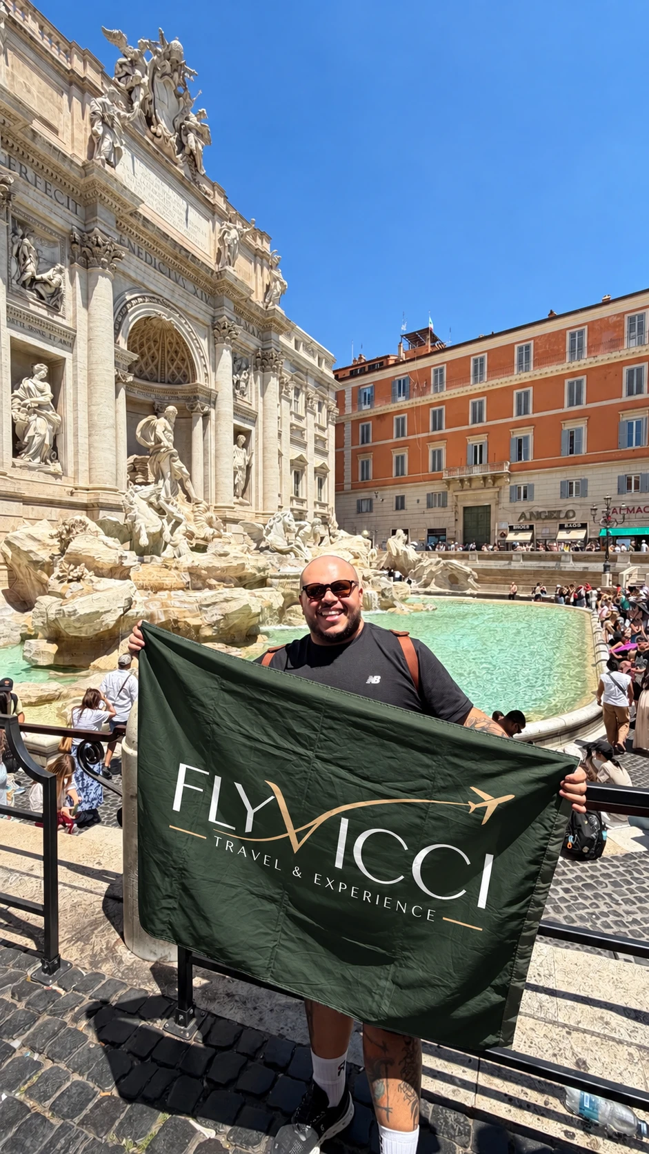 Lucas Rusty, fundador da FlyVicci, segurando a bandeira da agência em frente à Fontana di Trevi, em Roma
